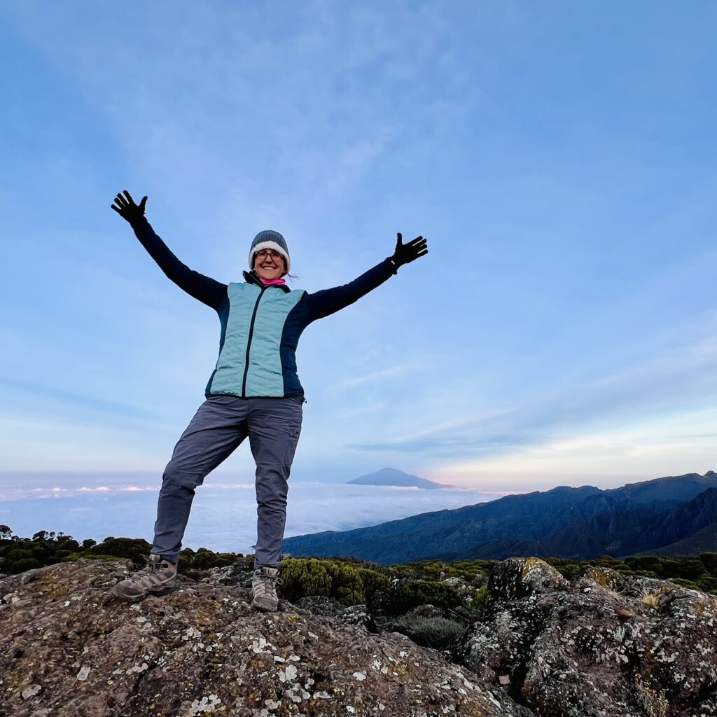 woman standing on mountain top with arms stretched out.